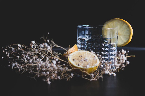 Boisson alcoolisée (gin et cocktail tonique) garnie de citron et de fleurs isolées sur fond noir. Cocktail glacé au citron et aux herbes. - Photo, image