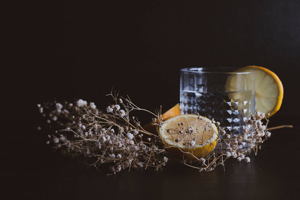 Alcohol drink (gin and tonic cocktail) garnished with lemon fruit and flower isolated on black background. Iced cocktail drink with lemon and herbs. - Photo, Image