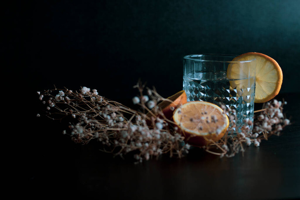 Bebida alcohólica (gin and tonic cocktail) adornada con fruta de limón y flor aislada sobre fondo negro. Bebida de cóctel helado con limón y hierbas. - Foto, Imagen