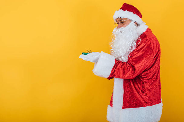 Santa Claus tiene un regalo sobre fondo amarillo. Concepto de Navidad - Foto, imagen