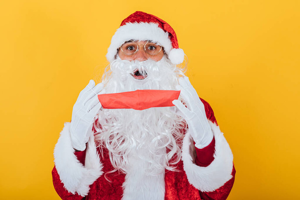Santa Claus putting on a red face mask, on yellow background. Christmas concept - Foto, Imagem