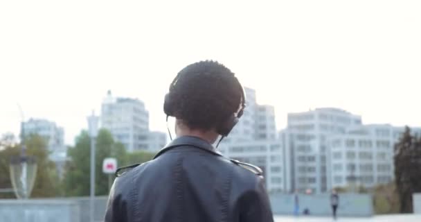 Портрет одинокой африканской молодой музыкантки-танцовщицы слушает песни с подогревающимися на улице наушниками, двигает своим телом ритмично выглядит в камере, стоит на городском фоне - Кадры, видео