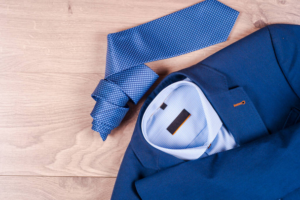 set of classic mens clothes - blue suit, shirts, brown shoes, belt and tie on wooden background. - Photo, Image