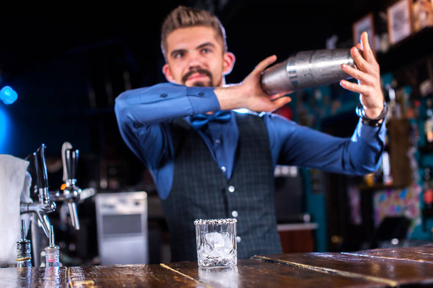 Эксперт-бармен делает коктейль, стоя возле барной стойки в пабе - Фото, изображение