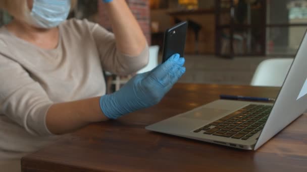 保護マスクと手袋を持つ女性の閉鎖は、カフェで電話を使用しています - 映像、動画