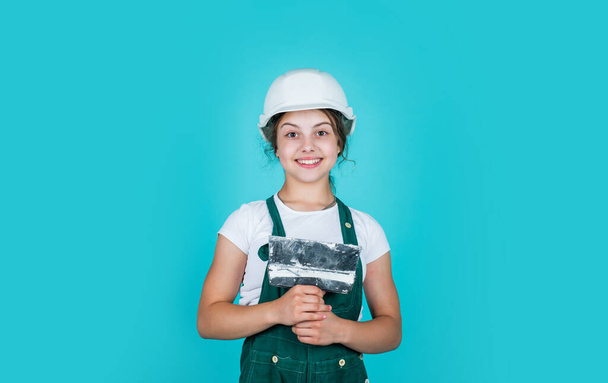 fixing everything. kid wear helmet on construction site. teen girl plasterer with tool spatula. child on repairing work. concept of renovation in workshop. busy professional carpenter with trowel - Foto, Imagen