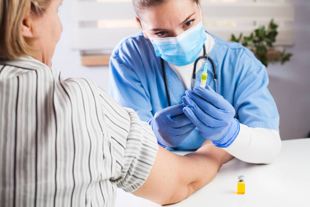 Lekarz rodzinny posiadający fiolkę z żółtym płynem, strzykawkę z zastrzykiem, szczepienie pacjenta w podeszłym wieku, koncepcja uodpornienia wirusa COVID-19, badanie kliniczne szczepionki - Zdjęcie, obraz