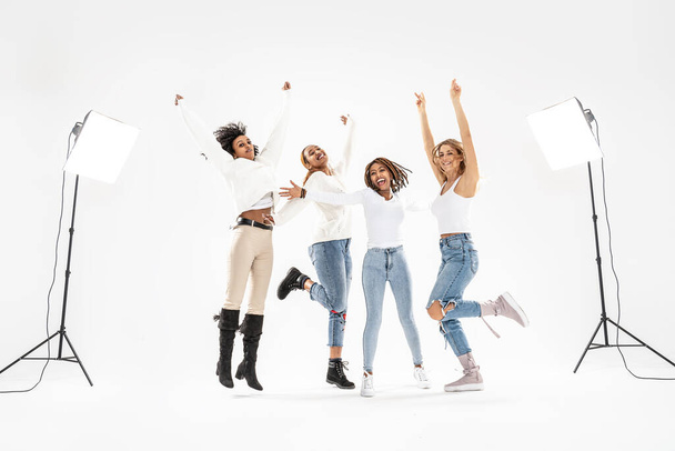 Four millennial multiethnic girlfriends jumping and laughing on white studio background. Happy young people lifestyle and friendship concept. - Фото, зображення