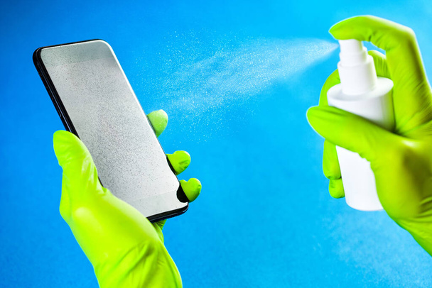 Hands in green gloves spraying antibacterial antiseptic sanitizer onto mobile phone screen,Coronavirus COVID-19 global pandemic crisis,protection and prevention from infection spreading & transfer - Photo, Image
