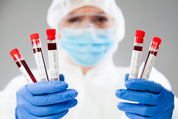 Εργαστηριακός επιστήμονας ή ιατρικός τεχνολόγος φορώντας προστατευτική στολή και μάσκα συγκράτησης κενού σωλήνα δοκιμής, δείγμα αίματος ασθενούς από τον ιό του Coronavirus, απεικόνιση ανάλυσης DNA νόσου του ιού COVID-19 PCR - Φωτογραφία, εικόνα