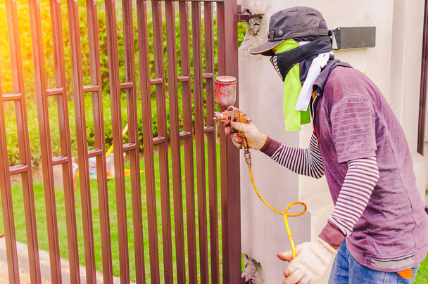 Gli operai stanno usando uno spruzzatore di vernice su una porta d'acciaio. I lavoratori devono proteggere la vernice spray dall'inalazione usando un panno per coprire il naso. - Foto, immagini