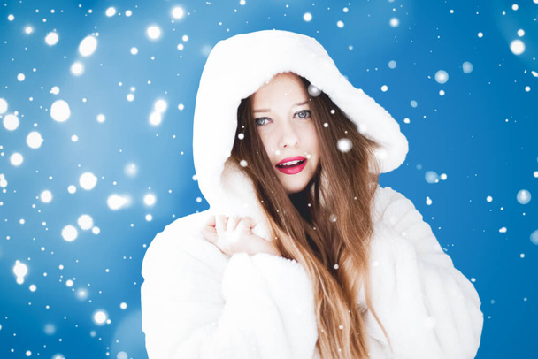 Feliz Navidad y vacaciones de invierno retrato de mujer joven con capucha blanca abrigo de piel, nieve sobre fondo azul, moda y estilo de vida - Foto, Imagen