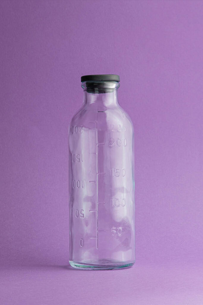 empty measuring bottle made of glass from a dropper on a purple background - Φωτογραφία, εικόνα
