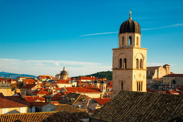Corazón del casco antiguo de Dubrovnik, campanario de la iglesia en la calle principal de Stradun, elevándose por encima de los tejados rojos de muchas pequeñas casas antiguas. Ciudad famosa por su patrimonio y la protección de la Unesco - Foto, Imagen