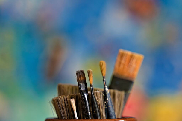Käytetty valikoima paintbrushes istuu purkissa hämärtynyt värillinen tausta.  - Valokuva, kuva