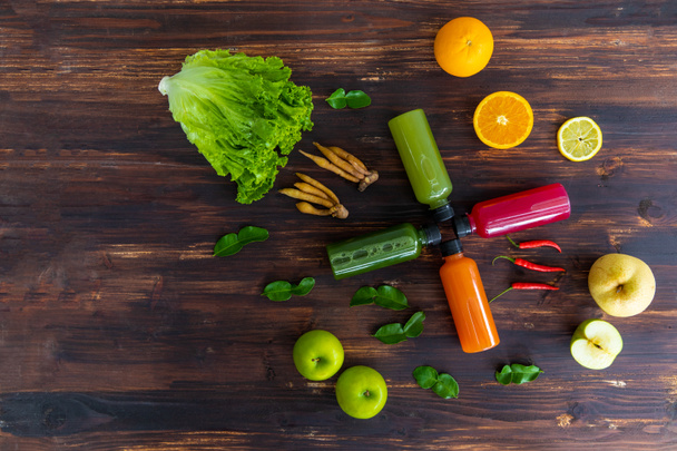 果物のスパイスと野菜が素朴な木製の背景に配置された冷間圧からの果物やハーブジュースのボトル。健康、デトックス、食事、代替食品や飲み物の概念. - 写真・画像