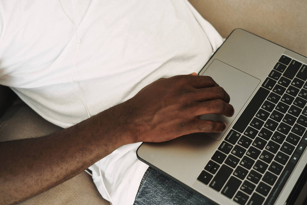 Uomo africano digitando testo sul computer portatile sul divano  - Foto, immagini