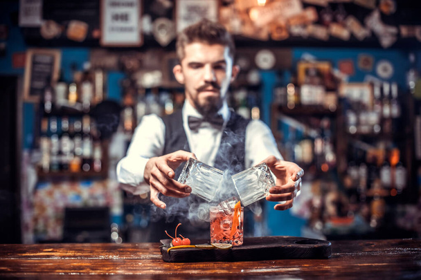 El barman confiado agrega ingredientes a un cóctel mientras está de pie cerca del mostrador del bar en la discoteca - Foto, Imagen