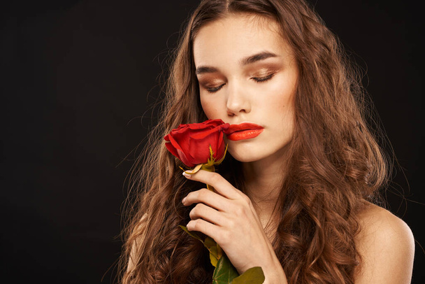 濃い背景のロングヘアメイクの赤い唇に赤いバラを持つ女性 - 写真・画像