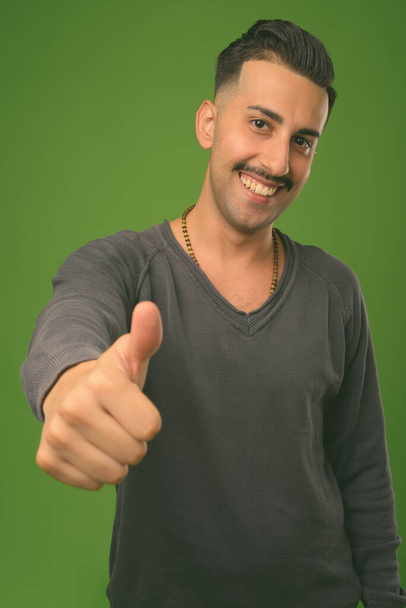 Young handsome Iranian man with mustache against green background - Photo, Image