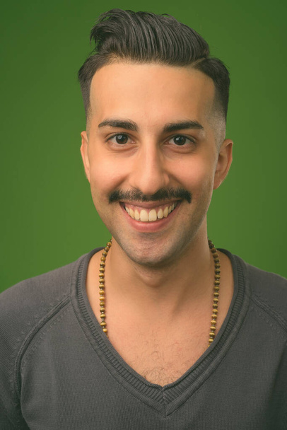 Young handsome Iranian man with mustache against green background - Fotoğraf, Görsel