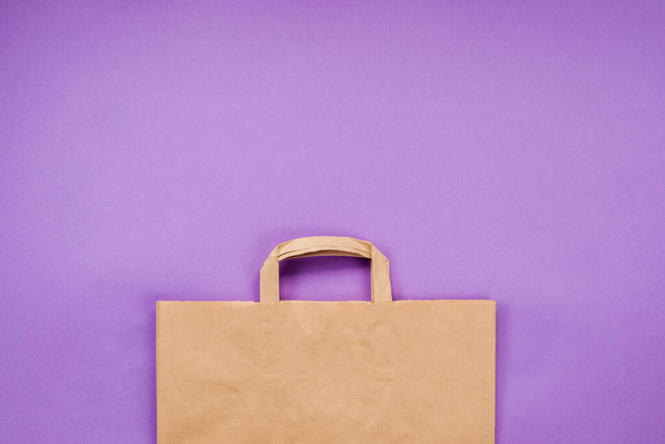 Craft paper shopping bag on the violet background. Copy space. - Foto, afbeelding