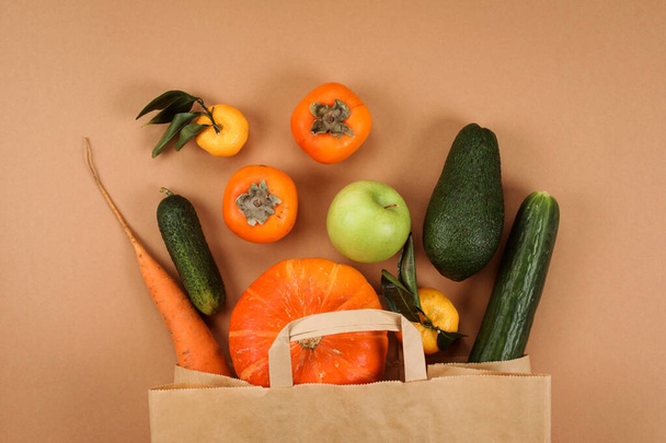 Green and orange vegetables in paper shopping bag on the beige background. - Foto, Imagem