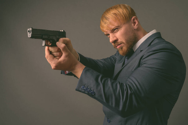 Uomo d'affari barbuto con pistola contro sfondo grigio - Foto, immagini