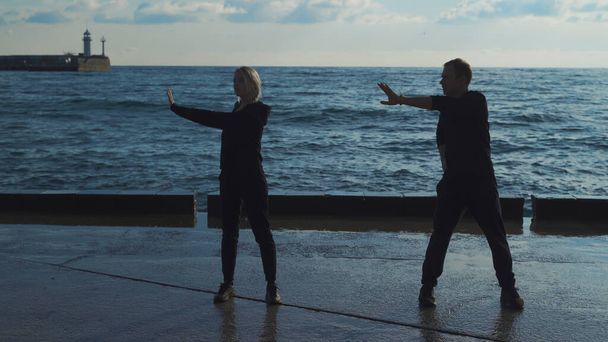 Young couple in sportswear are engaged in morning exercises against the background of the sea. The guy and the girl go in for sports together. - Foto, afbeelding