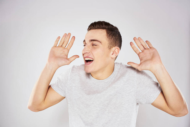 Hombre en una camiseta blanca emociones gestos con las manos de cerca recortado ver fondo de luz - Foto, imagen