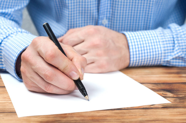 A mão escreve em uma folha de papel em branco. Empresário à mesa. - Foto, Imagem