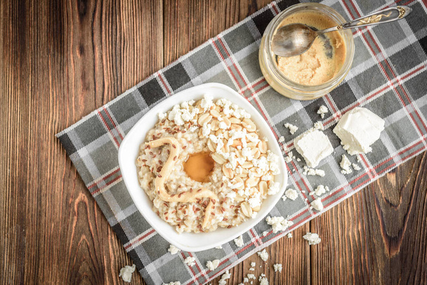 Hausgemachte Haferflocken mit Honig, Erdnussbutter, Erdnüssen, Leinsamen und Quark auf hölzernem Hintergrund. Gesundes Frühstück. - Foto, Bild
