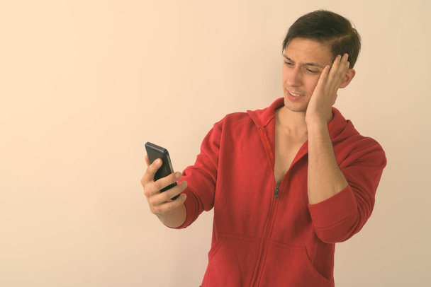 Студийный снимок молодого красивого мужчины, страдающего головной болью при использовании мобильного телефона на белом фоне - Фото, изображение