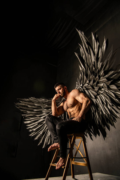 przystojny atletyczny mężczyzna w czarny anioł kostium na czarnym tle - Zdjęcie, obraz