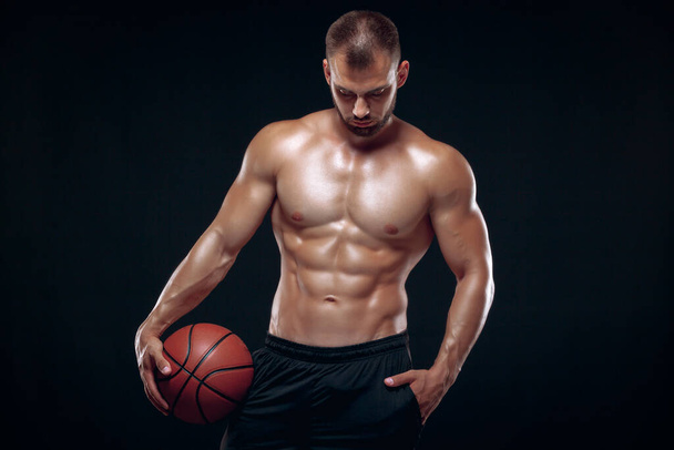 Portrait of a very muscular naked man playing basketball isolated on black background - Zdjęcie, obraz