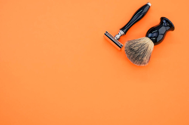 An overhead shot of a shaving brush and razor on orange background with space for your text - Foto, Imagem