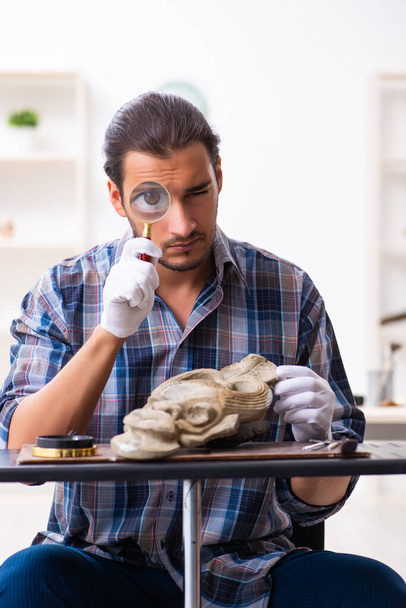 Genç erkek arkeolog eski Afrika taş maskesi üzerinde çalışıyor. - Fotoğraf, Görsel