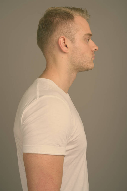 Mladý pohledný muž s blond vlasy proti šedému pozadí - Fotografie, Obrázek