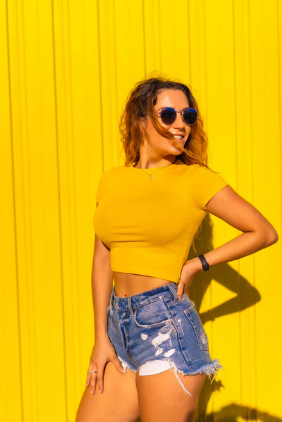 Lifestyle, Caucasian blonde girl in yellow t-shirts and short jeans on a yellow background. Fashionable posing with a smile, street photography - Photo, Image