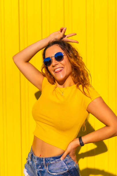 Lifestyle, Caucasian blonde girl in yellow shirts on a yellow background. Very happy and smiling and making the symbol of vistoria in hand - 写真・画像
