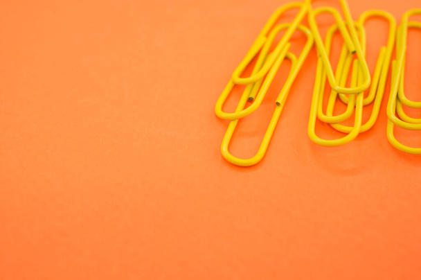 A closeup of yellow paperclips on orange background with space for your text - Fotografie, Obrázek