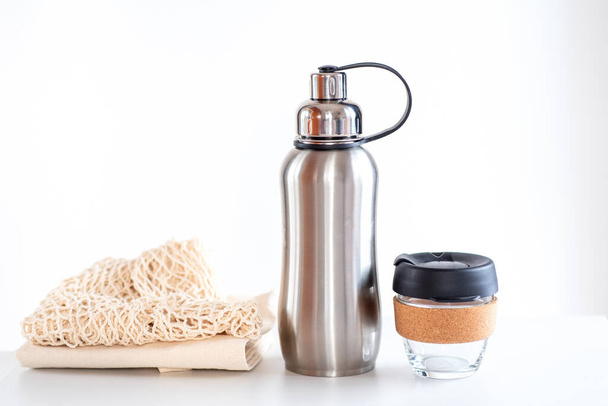 Экологичные сумки для покупок, многоразовая чашка кофе, стальная бутылка для воды на белом фоне. Устойчивая жизнь. - Фото, изображение