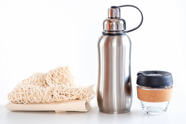 Экологичные сумки для покупок, многоразовая чашка кофе, стальная бутылка для воды на белом фоне. Устойчивая жизнь. - Фото, изображение