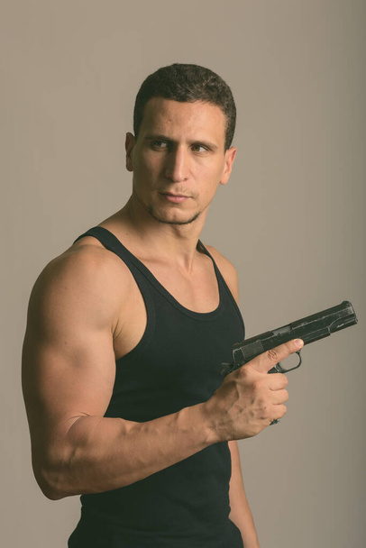 Студийный кадр молодого мускулистого перса, думающего, держа пистолет на сером фоне - Фото, изображение