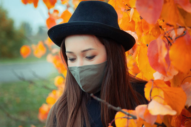 πορτρέτο ενός κοριτσιού με καπέλο και μάσκα στο φόντο ενός φθινοπωρινού δέντρου - Φωτογραφία, εικόνα