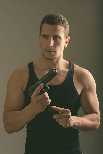 Studio shot of young muscular Persian man reloading gun while thinking in dark room - Photo, Image