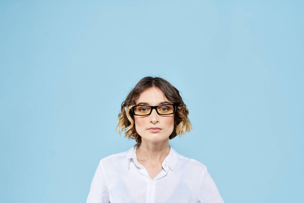 Mujer de negocios sobre un fondo azul gafas con bordes oscuros pelo rizado camisa ligera vista recortada - Foto, Imagen
