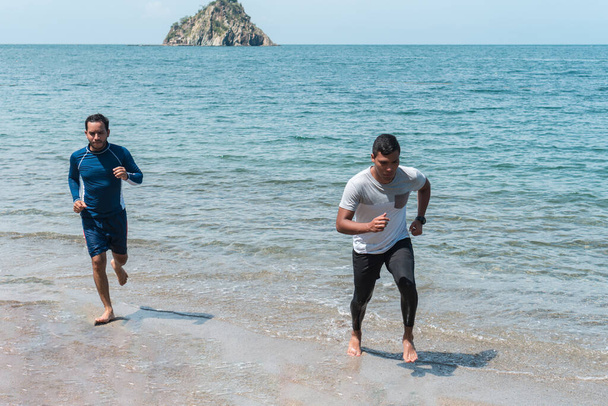 Kumsalda koşan iki adam. Erkek koşucular dışarıda antrenman yapıyor. - Fotoğraf, Görsel