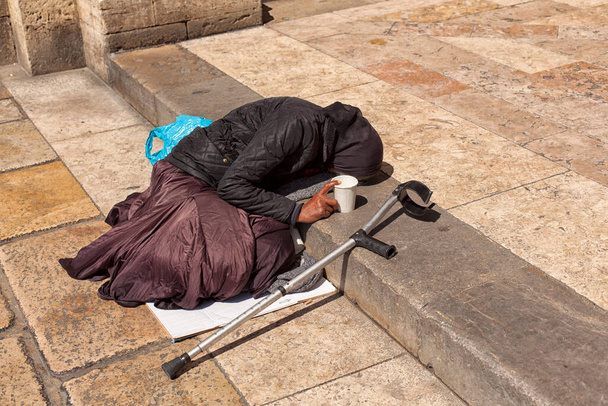 a beggar old woman lies on the steps in front of the entrance to the church - Photo, Image