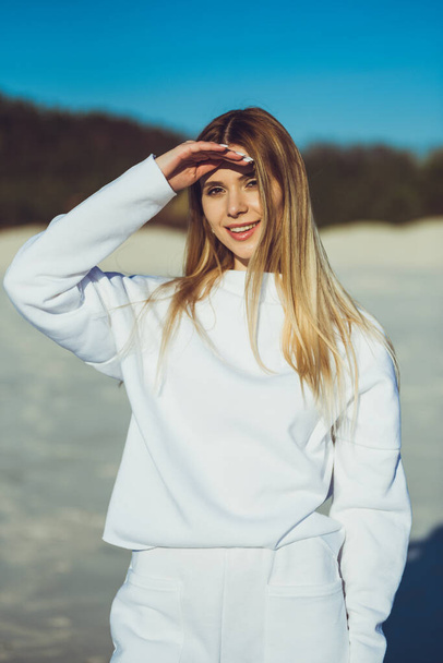 Portrait of beautiful blonde woman. Fashion woman wearing white warm clothes outdoor on the beach. - Фото, изображение